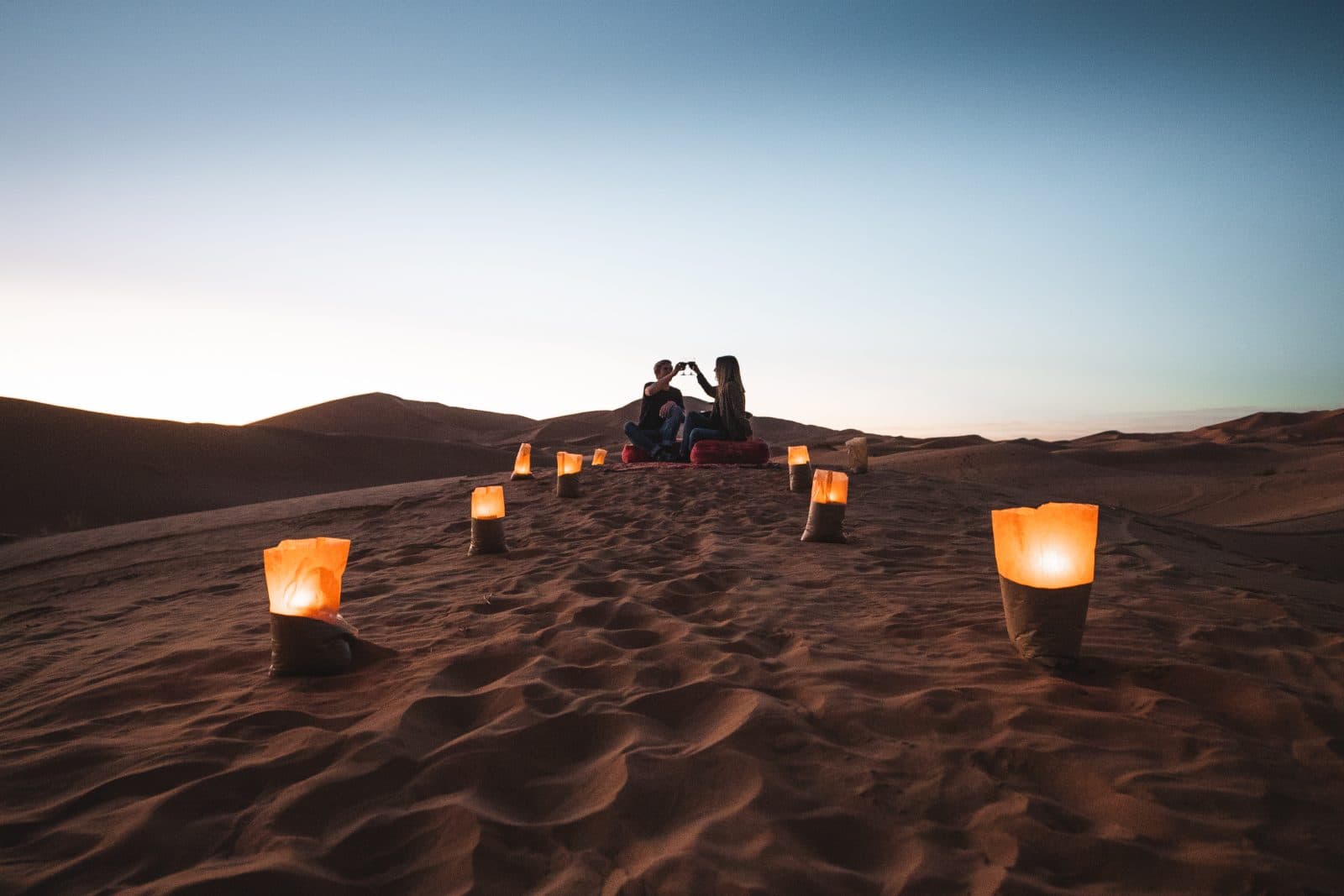 Guests toasting on a lantern-lit dune above Tiziri Camp at dusk